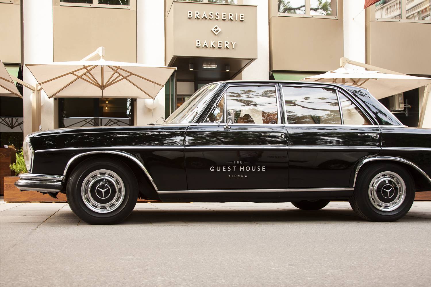 A black 1967 Mercedes 250 S parked on the side of a road, part of The Guesthouse Vienna's Classic Car Tour.
